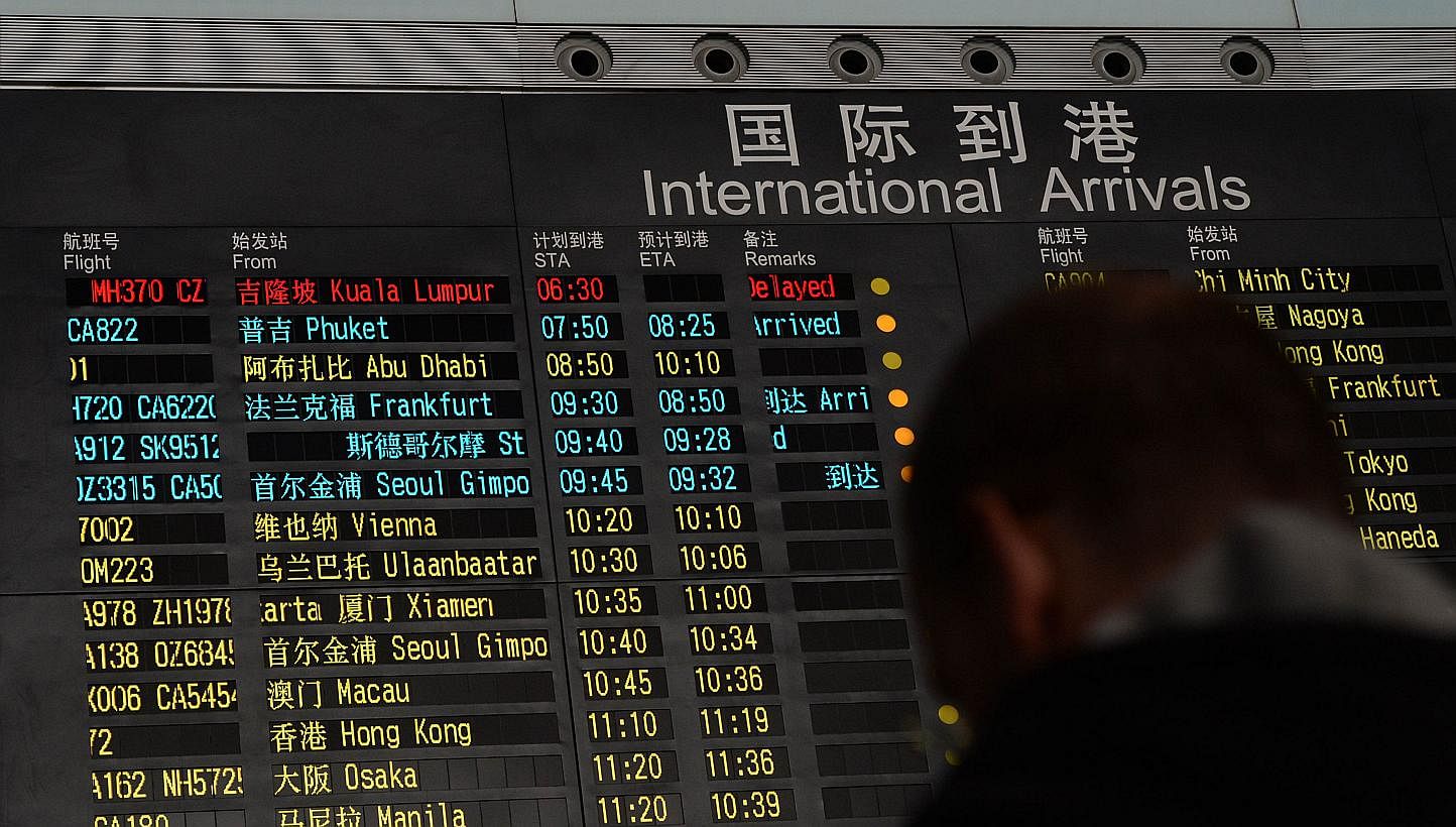 A man stands beside the arrival board showing the flight MH370 (top-red) at the Beijing Airport after news of the Malaysia Airlines Boeing 777-200 plane disapeared on March 8, 2014. -- PHOTO: AFP
