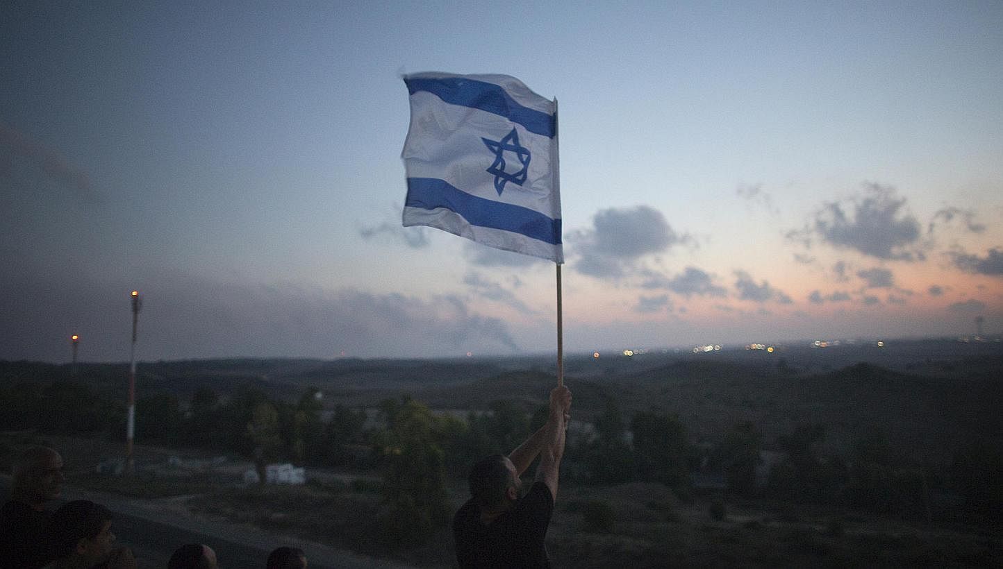 An Israeli man holds up a flag atop a hill overlooking the Gaza Strip in the southern town of Sderot on July 20, 2014. -- PHOTO: REUTERS