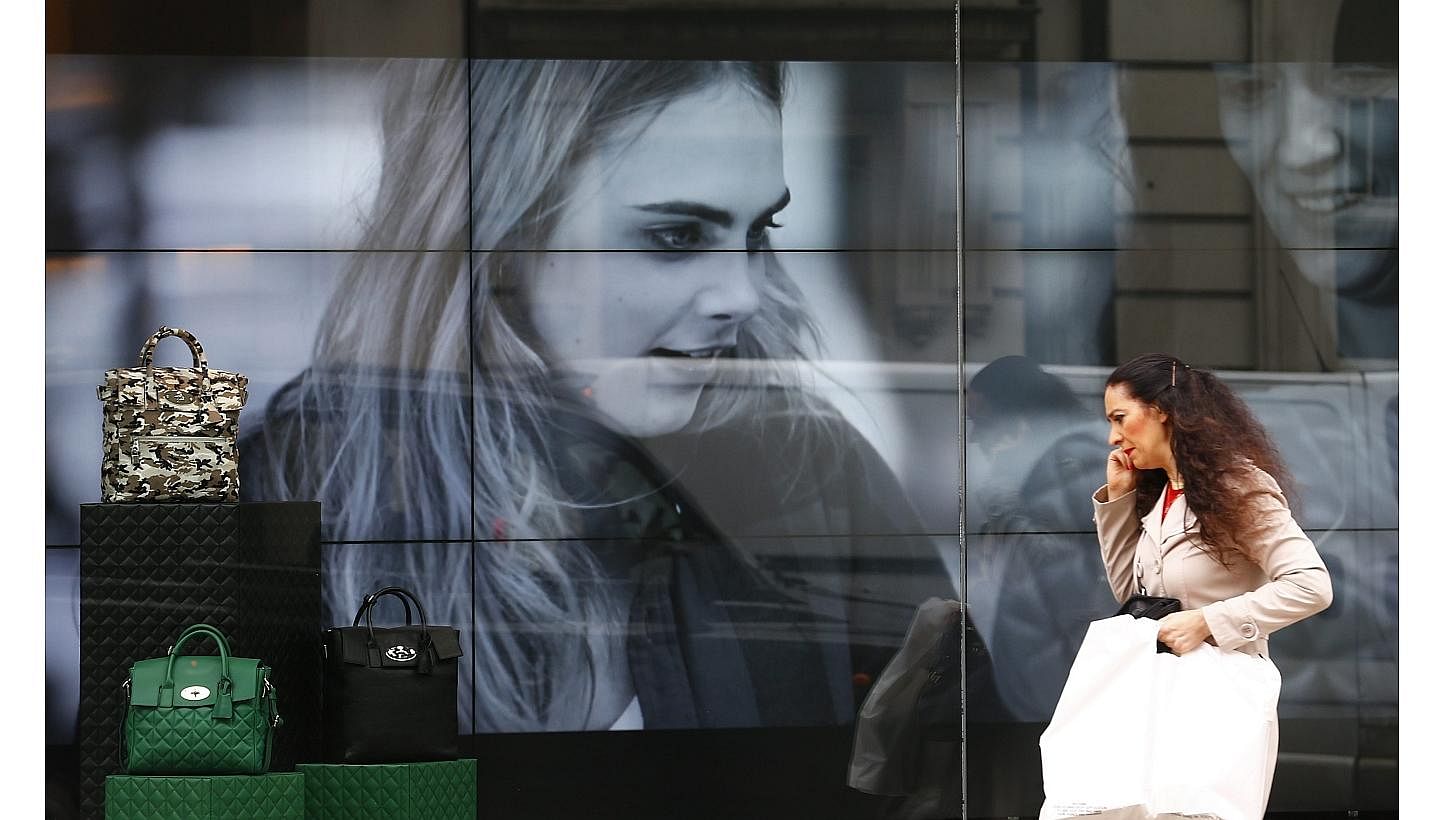 &nbsp;A woman walks past a video display in the shop window of a Mulberry store in central London on Oct 14, 2014.&nbsp;The ailing British luxury goods brand Mulberry has appointed Johnny Coca as its new creative director. -- PHOTO: REUTERS