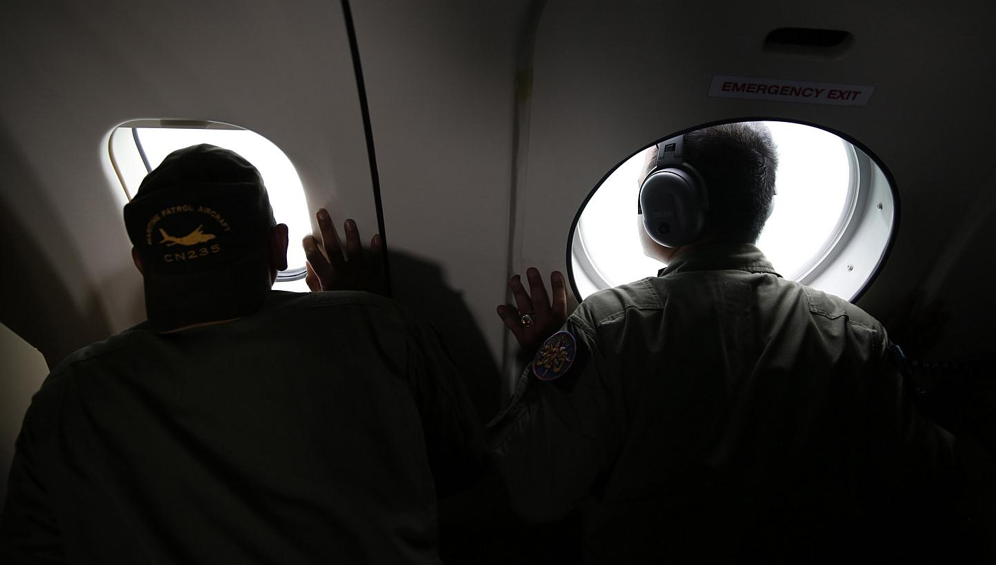 Crew members of an Indonesian Navy maritime surveillance plane look out windows during a search for wreckage and the remains of passengers onboard the AirAsia QZ8501 flight, over the Karimata Strait south of Pangkalan Bun, Central Kalimantan on Jan 1