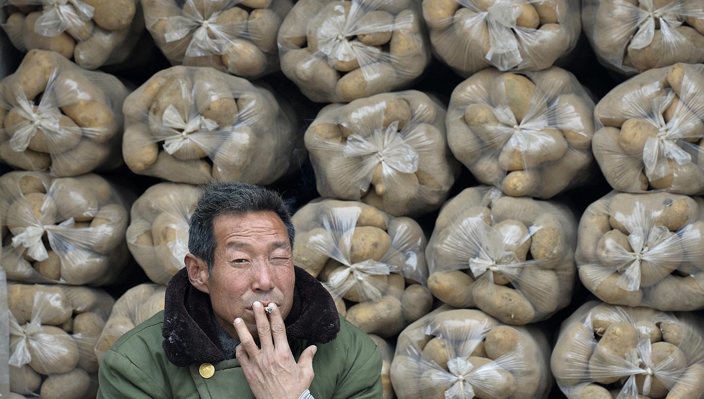 A vendor smokes a cigarette in front of sacks of potatoes piled up on a truck at a whole sale market in Taiyuan, Shanxi province in this Feb 17, 2014 file photo. -- PHOTO: REUTERS
