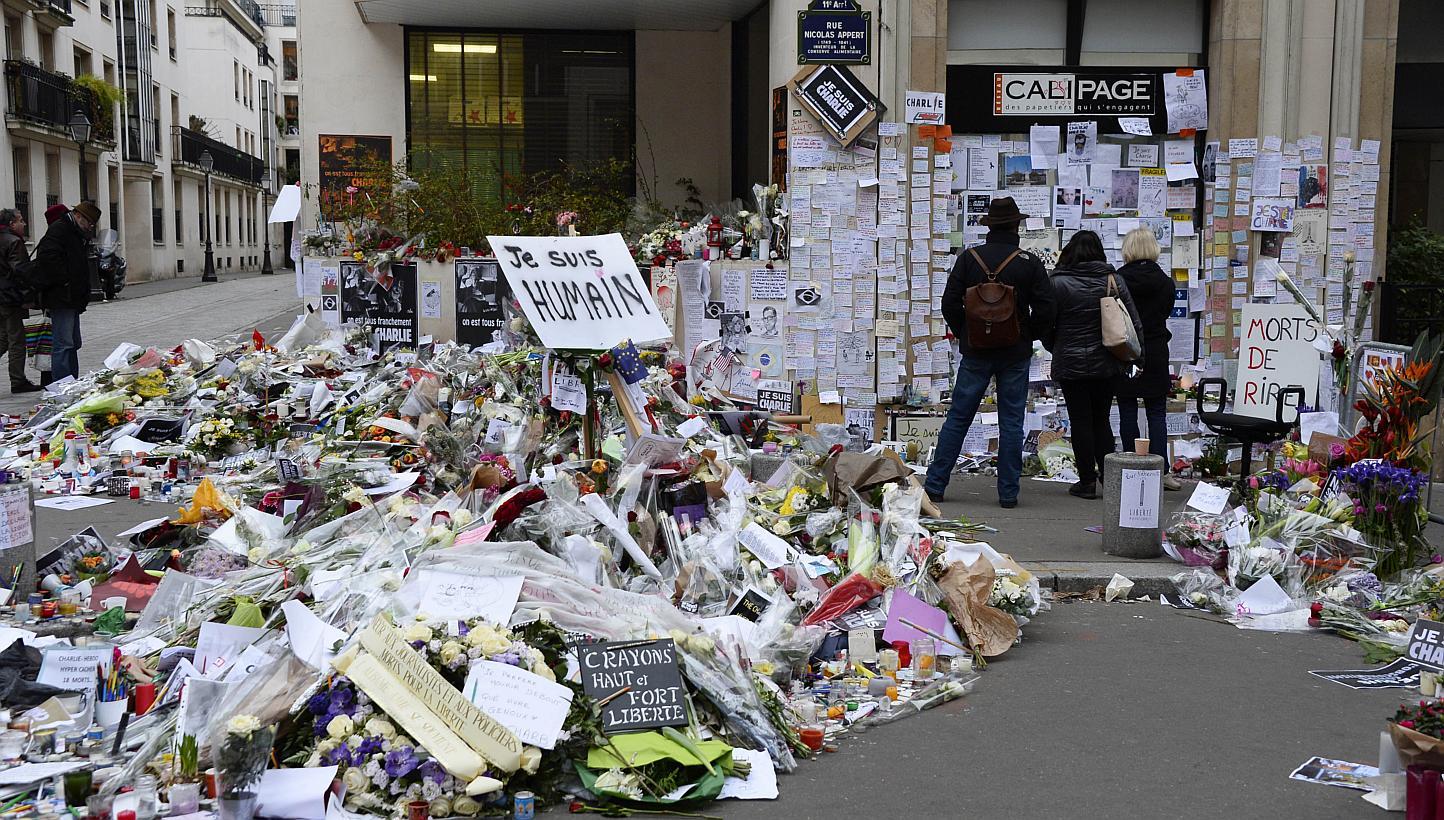 People visit a makeshift memorial near the Paris headquarters of the French satirical weekly Charlie Hebdo on Jan 12, 2015, in tribute to the 17 victims of a three-day killing spree by homegrown Islamists. This week's edition will defiantly feat
