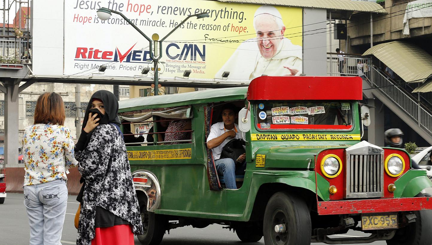 Filipino passengers wait for a jeepney, a popular and uniquely Filipino mode of mass transport, next to a giant Pope Francis billboard in Manila, Philippines on Jan 12, 2015.&nbsp;The Pope will travel in one during his visit to the country later this