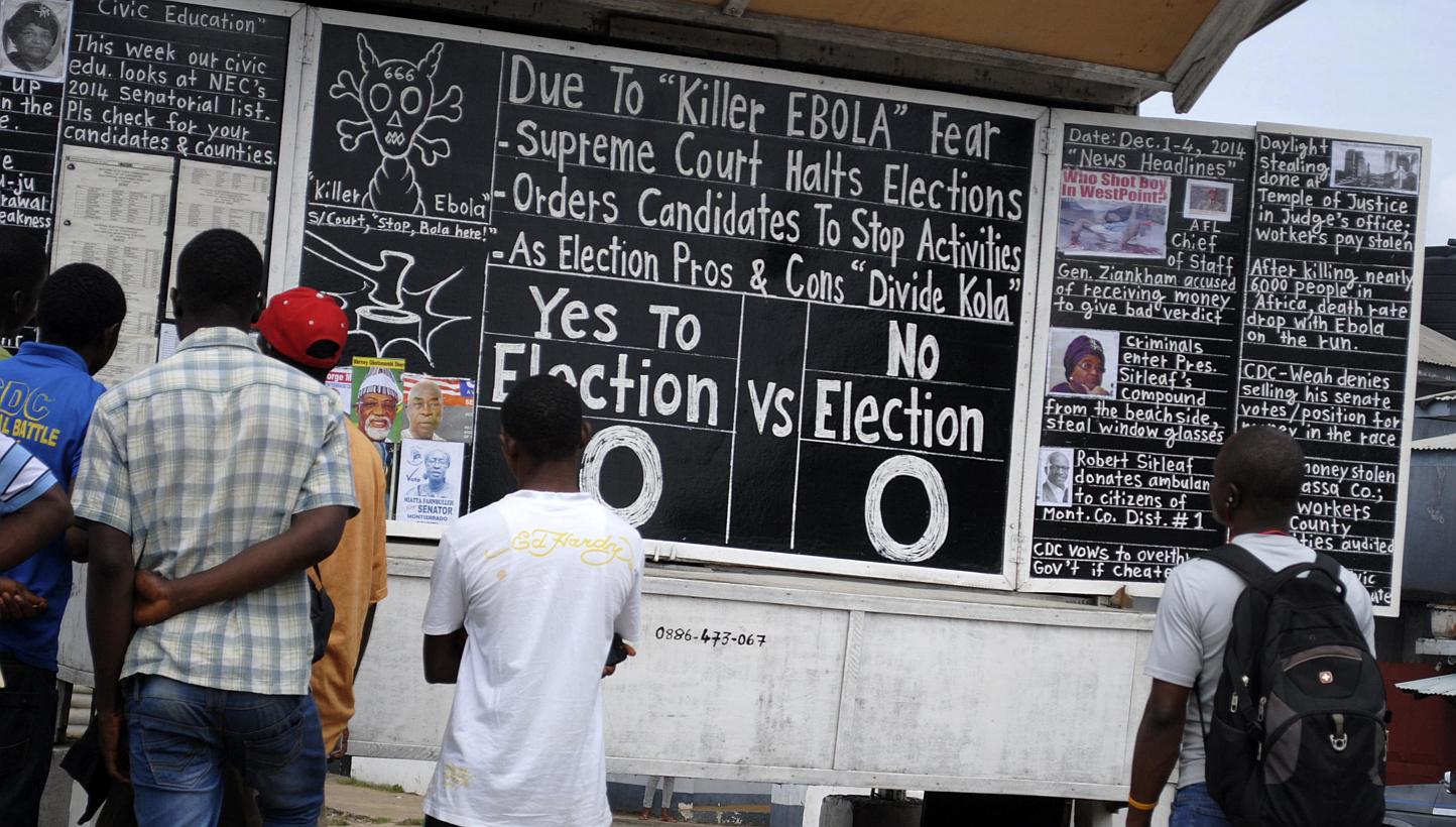 Bystanders read the headlines illustrating the battle over the holding of elections in Liberia amid the Ebola crisis at a street side chalkboard newspaper in Monrovia, Dec 2, 2014. -- PHOTO: REUTERS