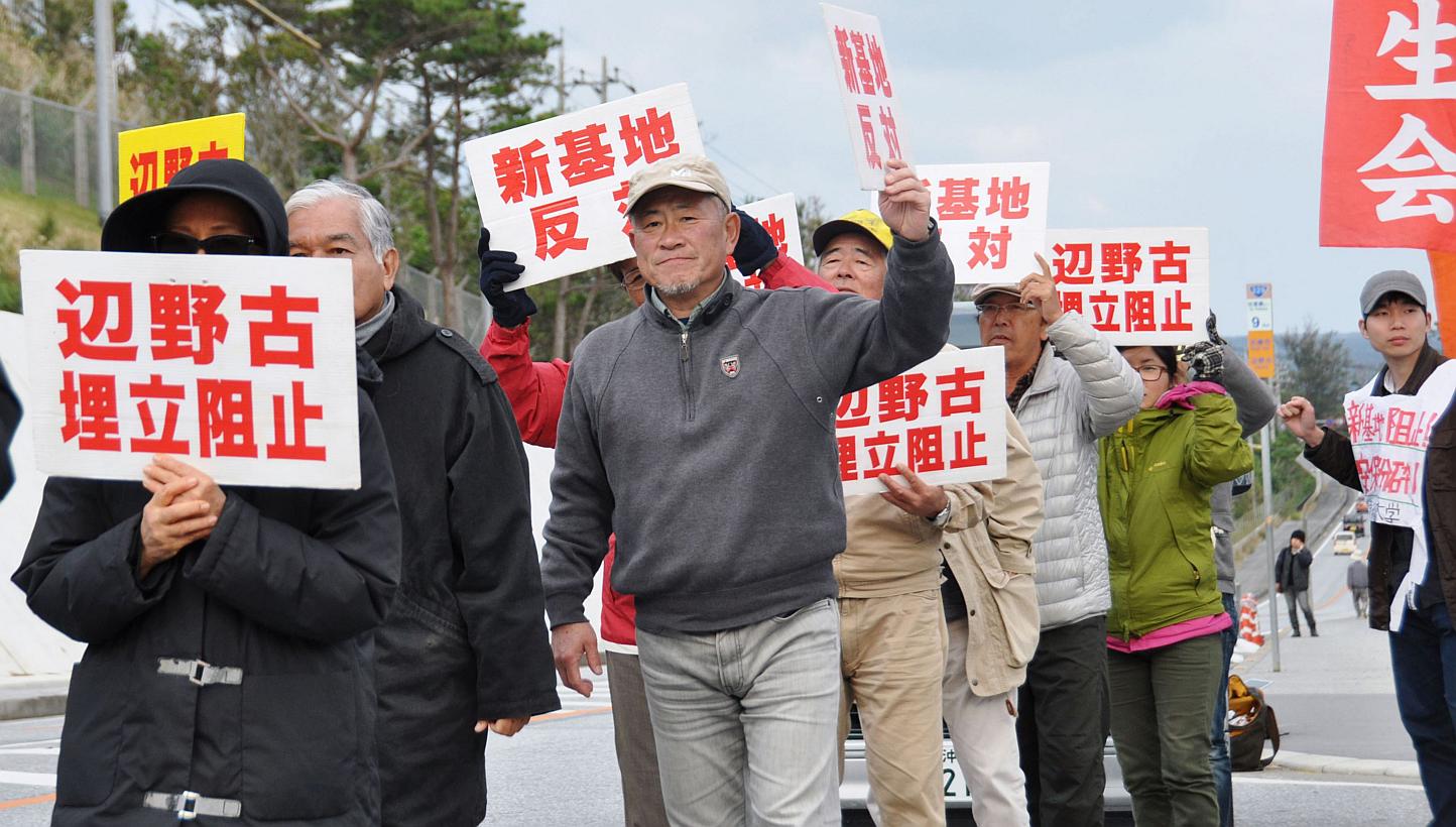 Anti-base activists hold signs reading "Stop landfill at Henoko" and "No new base", in front of a gate of the US Marine Corps' Camp Schwab at the tiny hamlet of Henoko in Nago on the southern Japanese island of Okinawa on Jan 15 in this photo taken b