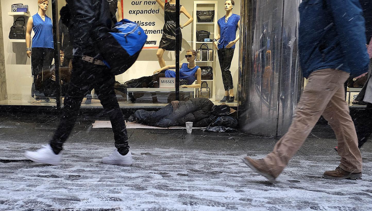 A homeless person sleeps on the sidewalk during a snow storm in New York on Jan 26, 2015. -- PHOTO: AFP