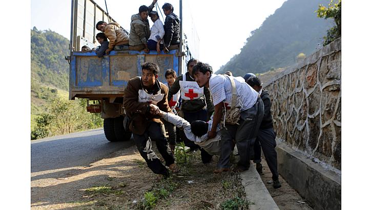 Volunteers of Myanmar Red Cross organisation carry wounded volunteer Moe Kyaw, 45, as the war victims fleeing from Laukkai sit on the truck after vehicles of rescue convoy were attacked by Kokang rebels near self-administered Kokang capital Laukkai, 