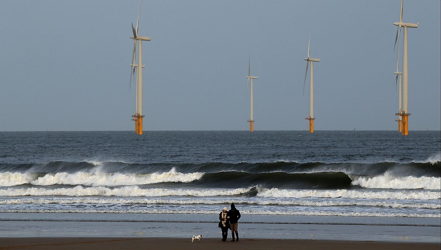 A couple walk their dog on Redcar beach past an offshore wind farm in Redcar, northeast England last month. -- PHOTO: REUTERS