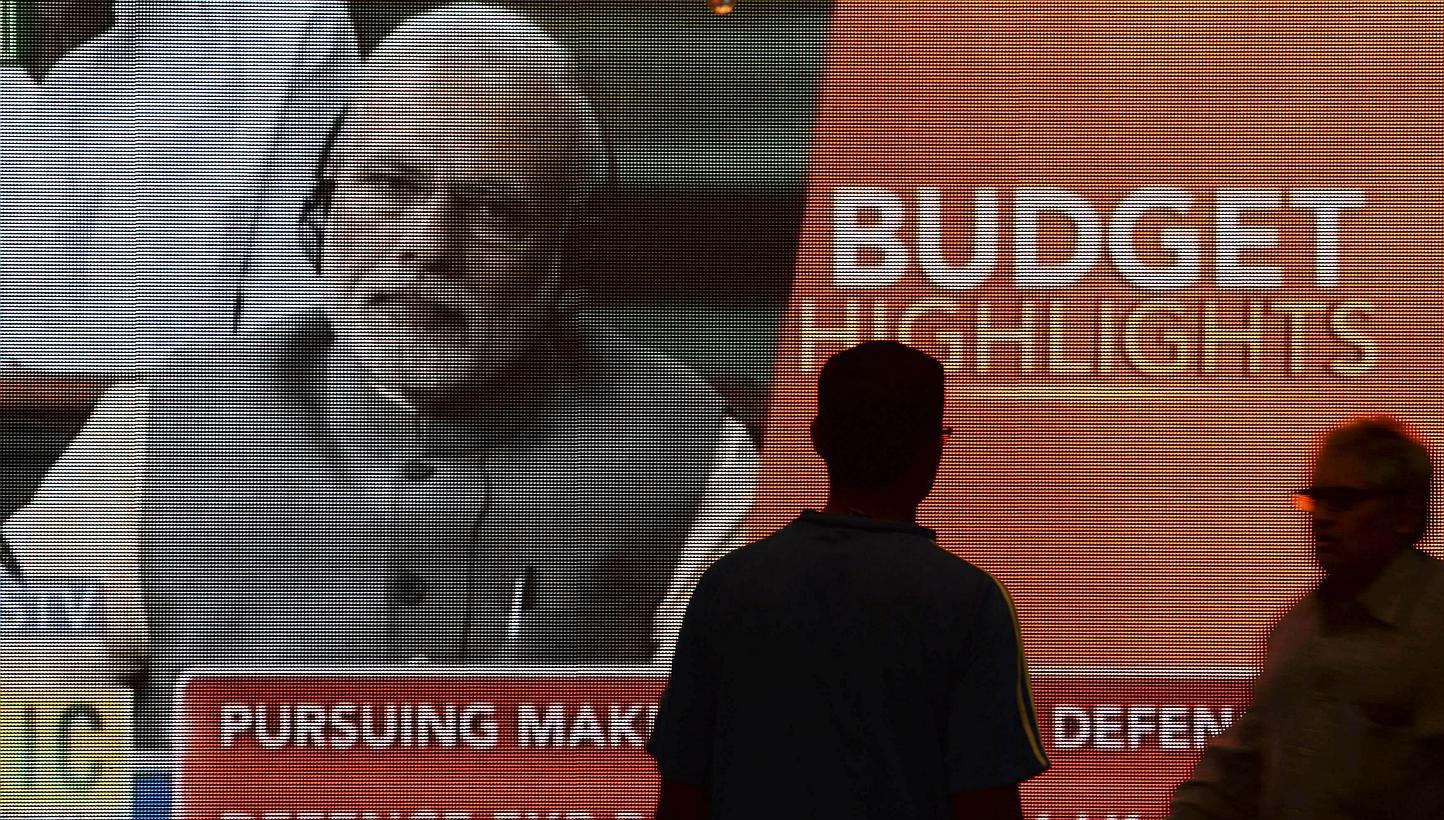 Indian office workers walk past a digital screen showing Prime Minister Narendra Modi listening to Finance Minister Arun Jaitley deliver his Budget speech at Parliament, in Mumbai on Feb 28, 2015. India's reform-minded prime minister appears to
