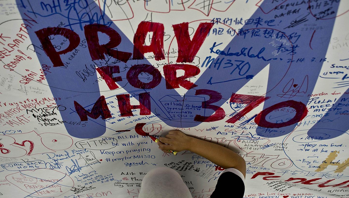 A file photo taken on March 14, 2014 shows a Malaysia Airlines employee writing a message expressing prayers and good wishes for passengers onboard missing Malaysia Airlines Flight MH370 at Kuala Lumpur International Airport in Sepang. -- PHOTO: AFP