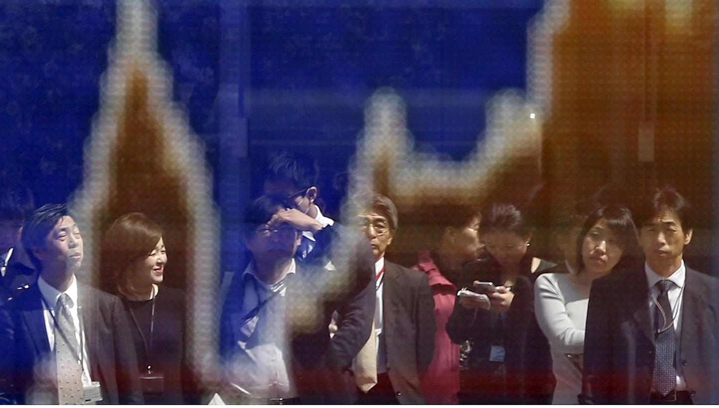 Passers-by are reflected on a graph showing Japan's Nikkei index outside a brokerage in Tokyo on March 30, 2015. -- PHOTO: REUTERS