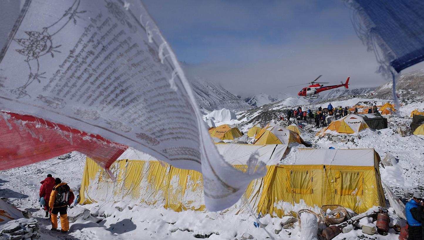 This April 26, 2015, photo shows Buddhist prayer flags fluttering in the wind near tents as a rescue helicopter takes off from Everest Base Camp, after an earthquake-triggered avalanche crashed through parts of the base camp, killing scores of people