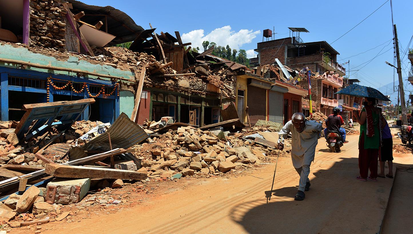 People walking past damaged houses at Trishuli in Nuwakot district north of Kathmandu on May 4, 2015. Nepali police and local volunteers found the bodies of about 100 trekkers and villagers buried in an avalanche set off by last month's devastating e
