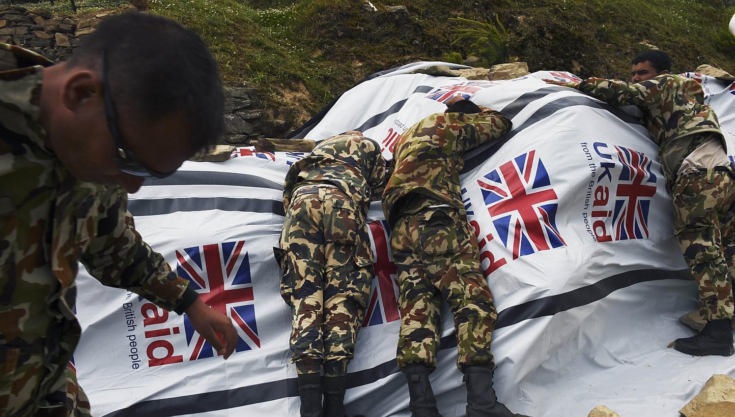 Nepali soldiers lay on a tarp covering food aid as they try to protect it from the rotor wash created by a Chinese transport helicopter during relief operations in the north-central village of Dunche in Nepal. Nepal's government said on Sunday, May 1
