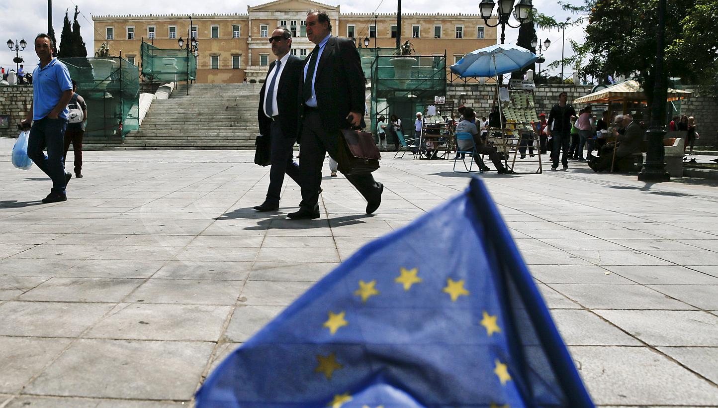 People make their way past a small European Union flag on Constitution (Syntagma) Square, with the parliament building seen in the background, in Athens on May 11, 2015. -- PHOTO: REUTERS 