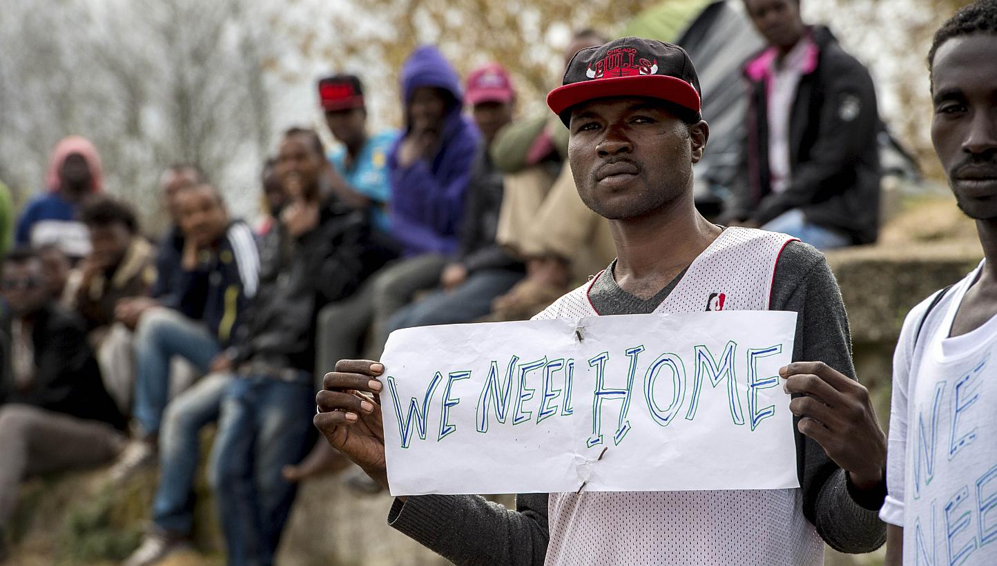 A migrant holds a sign reading "We need a home" during a visit by the French interior minister to their shelter in Calais, northern France, on May 4, 2015. -- PHOTO: AFP