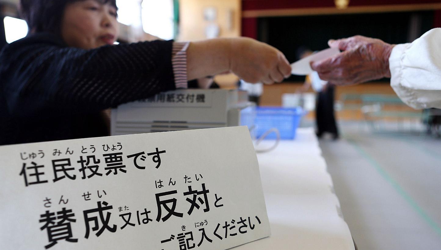 A resident (right) receives a ballot at a polling station in Osaka on May 17, 2015 to vote on a referendum to reform the city administration into a metropolitan government.&nbsp;The people of Japan's second city Osaka narrowly voted down Sunday a pla
