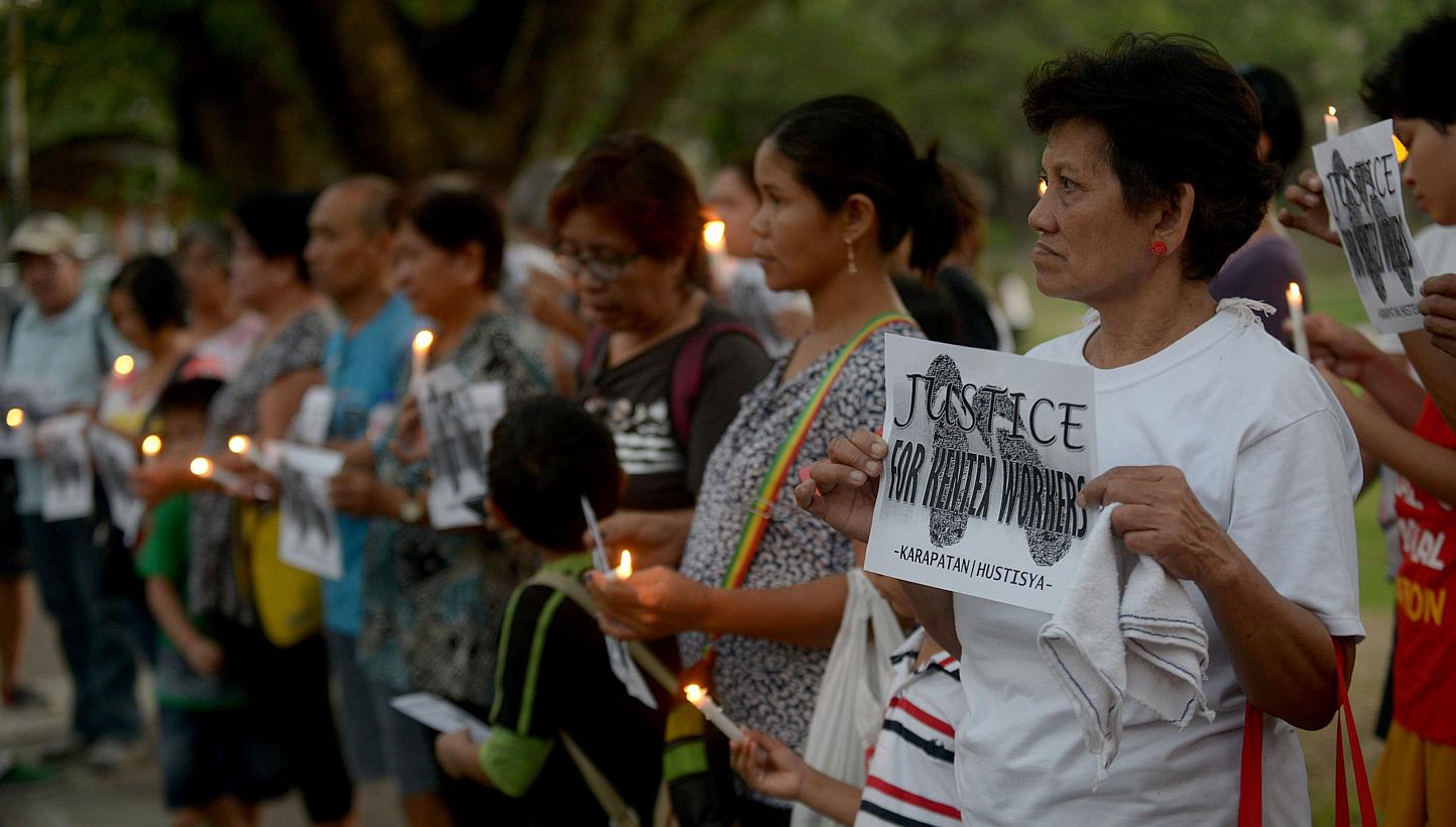 Activists hold candles and placards during a rally in Manila on May 16, 2015 for the victims of a fire that gutted a footwear factory on May 13. Philippine officials called on Sunday, May 17, for criminal penalties for factory owners who violate