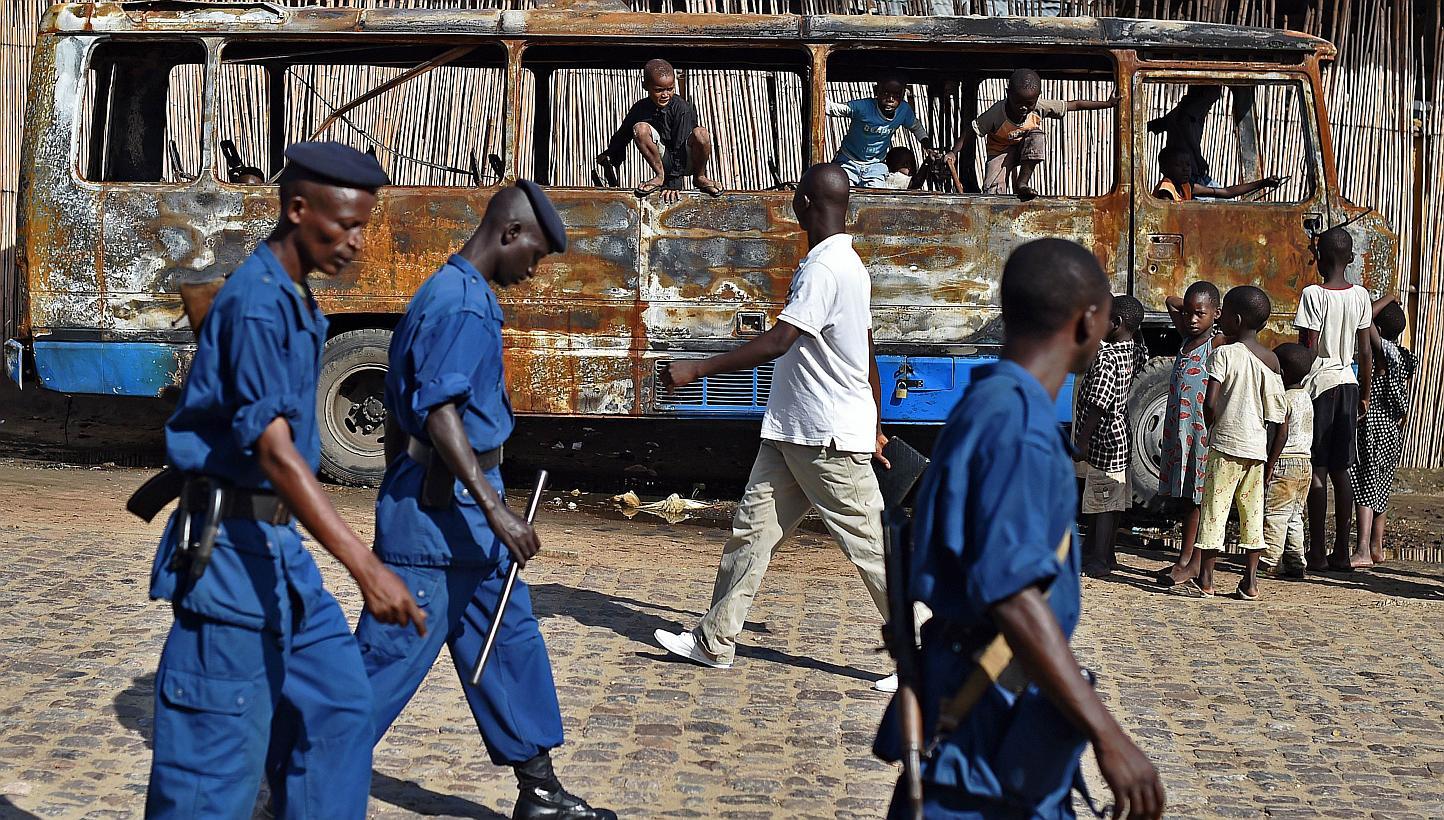 Children playing in a bus, burned out during protests, as policemen walk past in Bujumbura, Burundi, on May 17, 2015. -- PHOTO: AFP