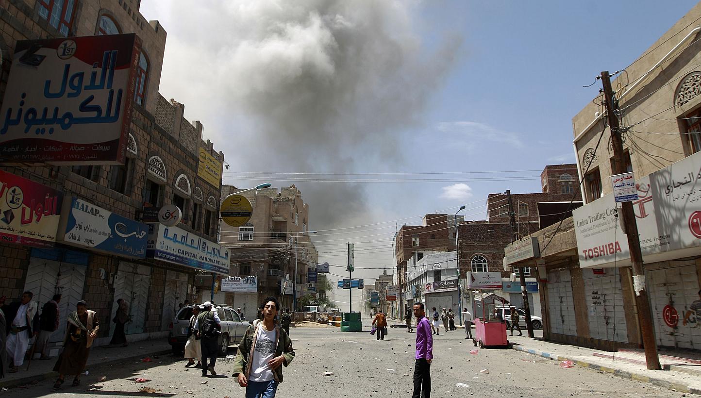 Yemeni men stand on a street as smoke billows following reported air strikes on the residence of Yemen's former president Ali Abdullah Saleh on May 10, 2015, in the capital Sana'a. Saudi-led coalition warplanes resumed strikes on the preisdienti