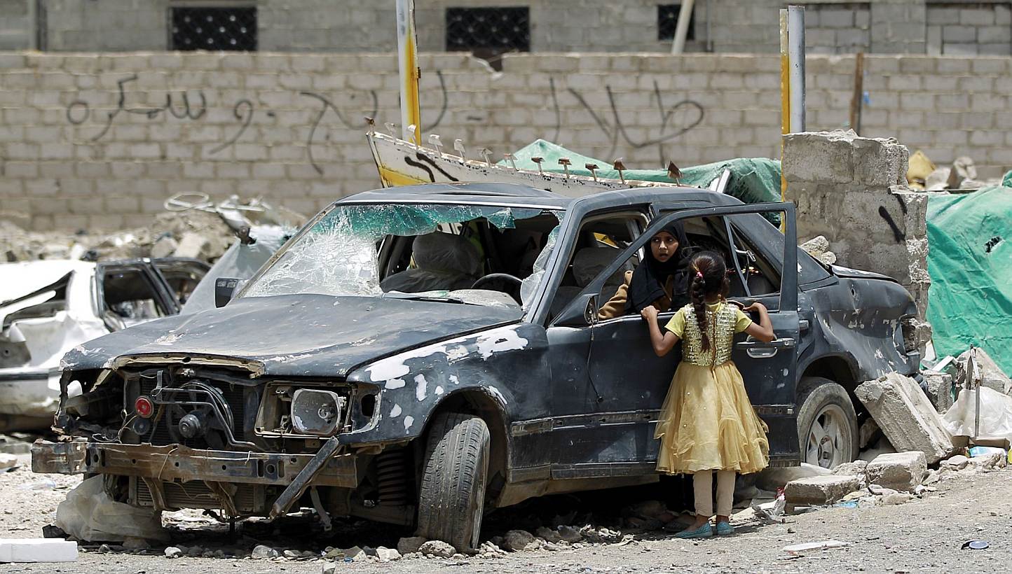 A Yemeni woman inpecting a damaged car in a residential area that was destroyed by Saudi-led air strike last month, in the capital Sanaa, on May 18, 2015. -- PHOTO: AFP