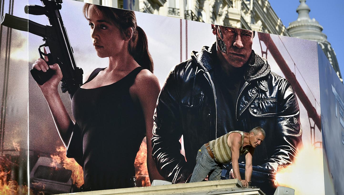 A worker is seen in front of a poster of Terminator Genisys showing cast members Arnold Schwarzenegger (right) and Emilia Clarke (left) at the Carlton Hotel, ahead of the 68th Cannes Film Festival, in Cannes, France, 12 May 2015. -- PHOTO: EPA
