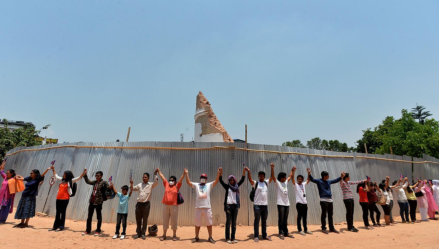 Nepalese people hold hands as they stand around the collapsed Dharahara Tower in Kathmandu on May 25, 2015, as the country marks one month since a deadly earthquake struck the country, killing more than 8,600 people. -- PHOTO: AFP