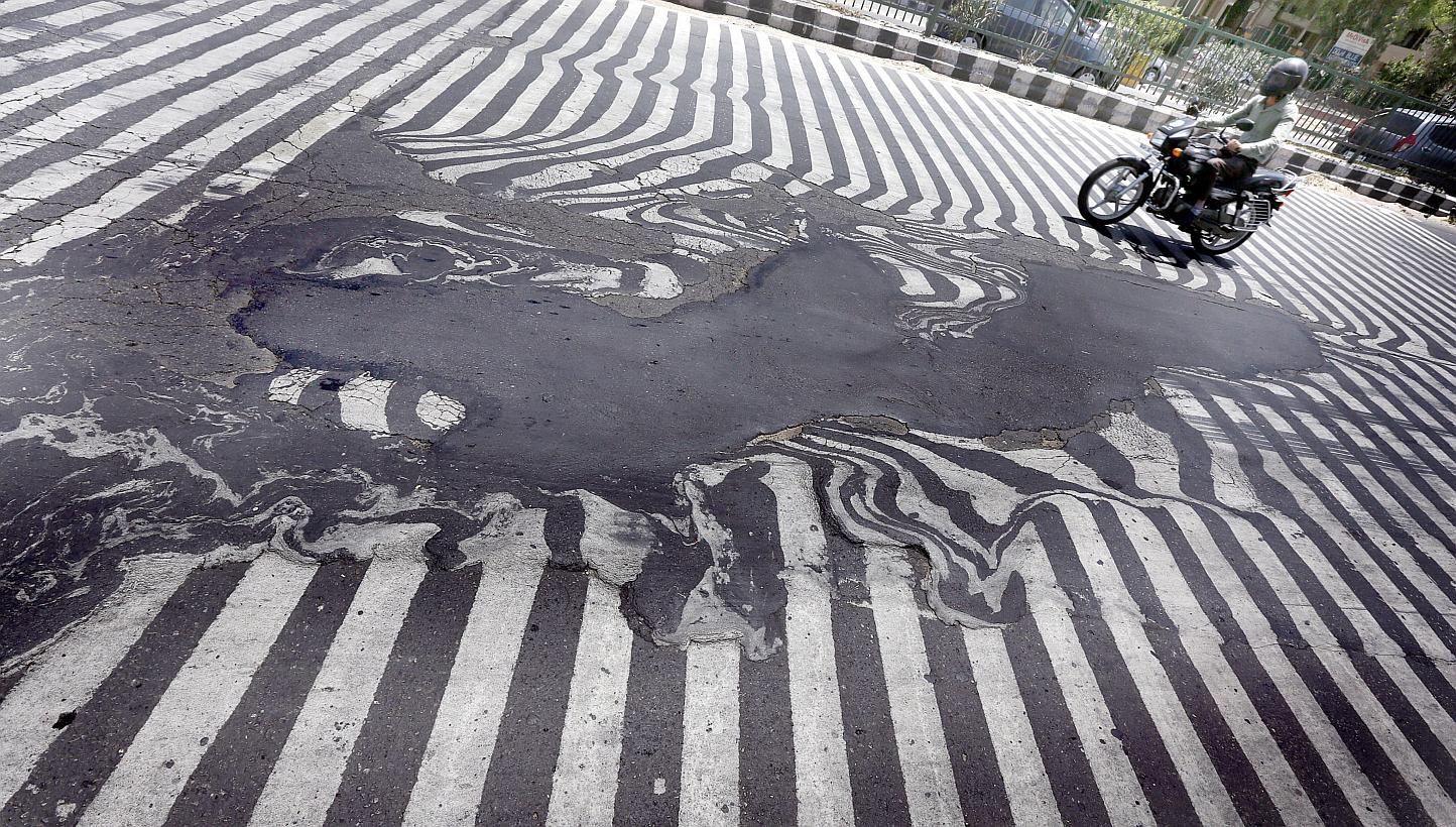 A motorcyclist rides past road markings that appear distorted due to the road asphalt melting and beginning to run, in New Delhi on May 27, 2015. Indian authorities have cancelled doctors' leave to help cope with the sick, as a heat wave spread acros