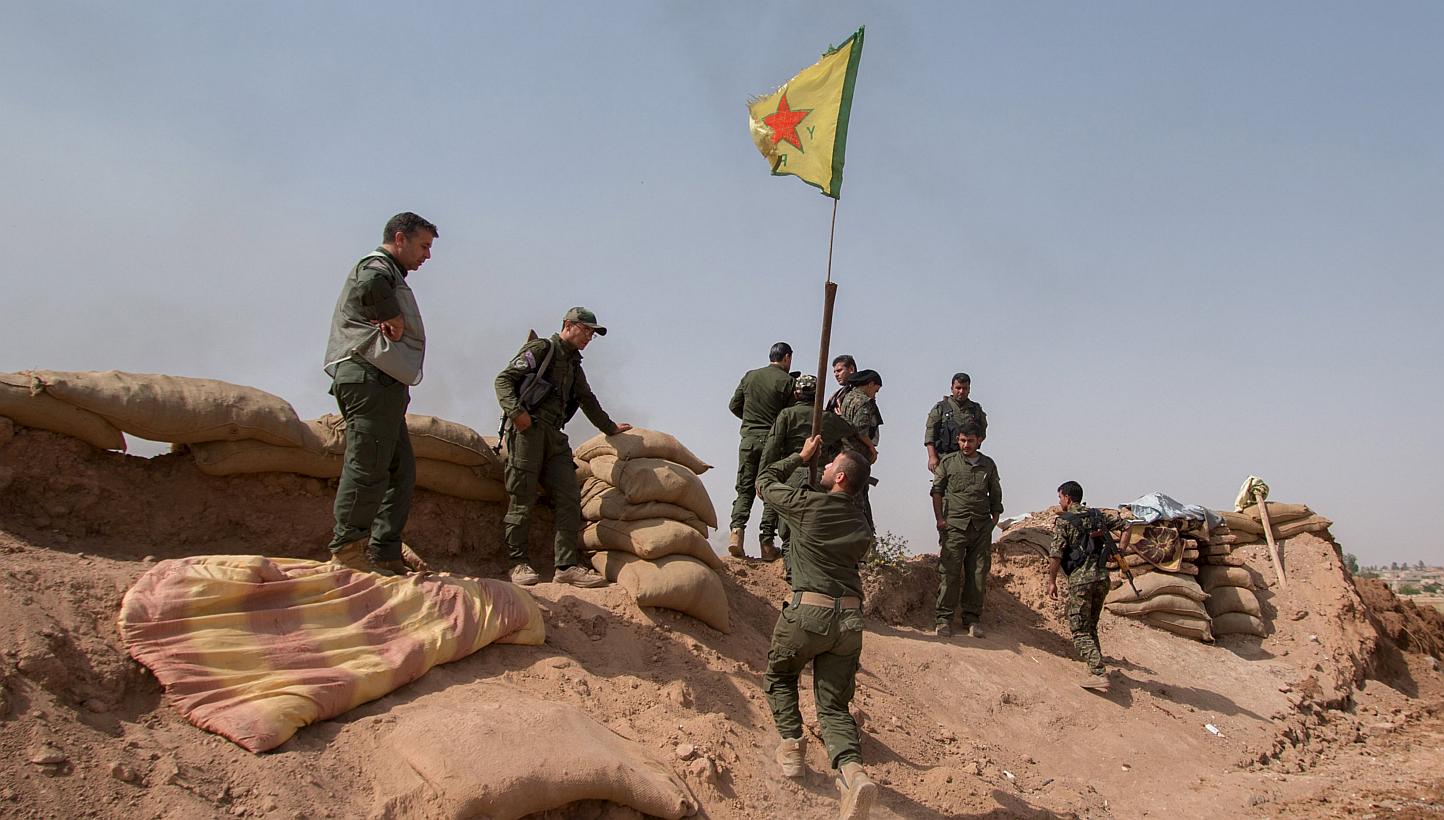Kurdish People's Protection Unit (YPG) fighters raise a YPG flag over a barrier in Tel al-Aghbish village, which they said they retook control of from the Islamic State in Iraq and Syria (ISIS) on May 21, 2015. A group monitoring the war on Wednesday