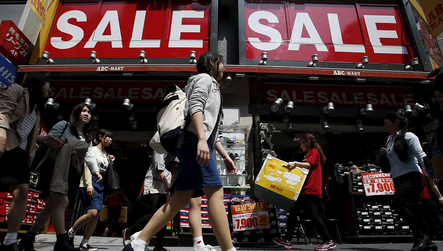 A shop clerk (second, right) carrying a box of shoes under sale signboards at a shoes retail store at a shopping district in Tokyo, Japan, on April 28, 2015. -- PHOTO: REUTERS