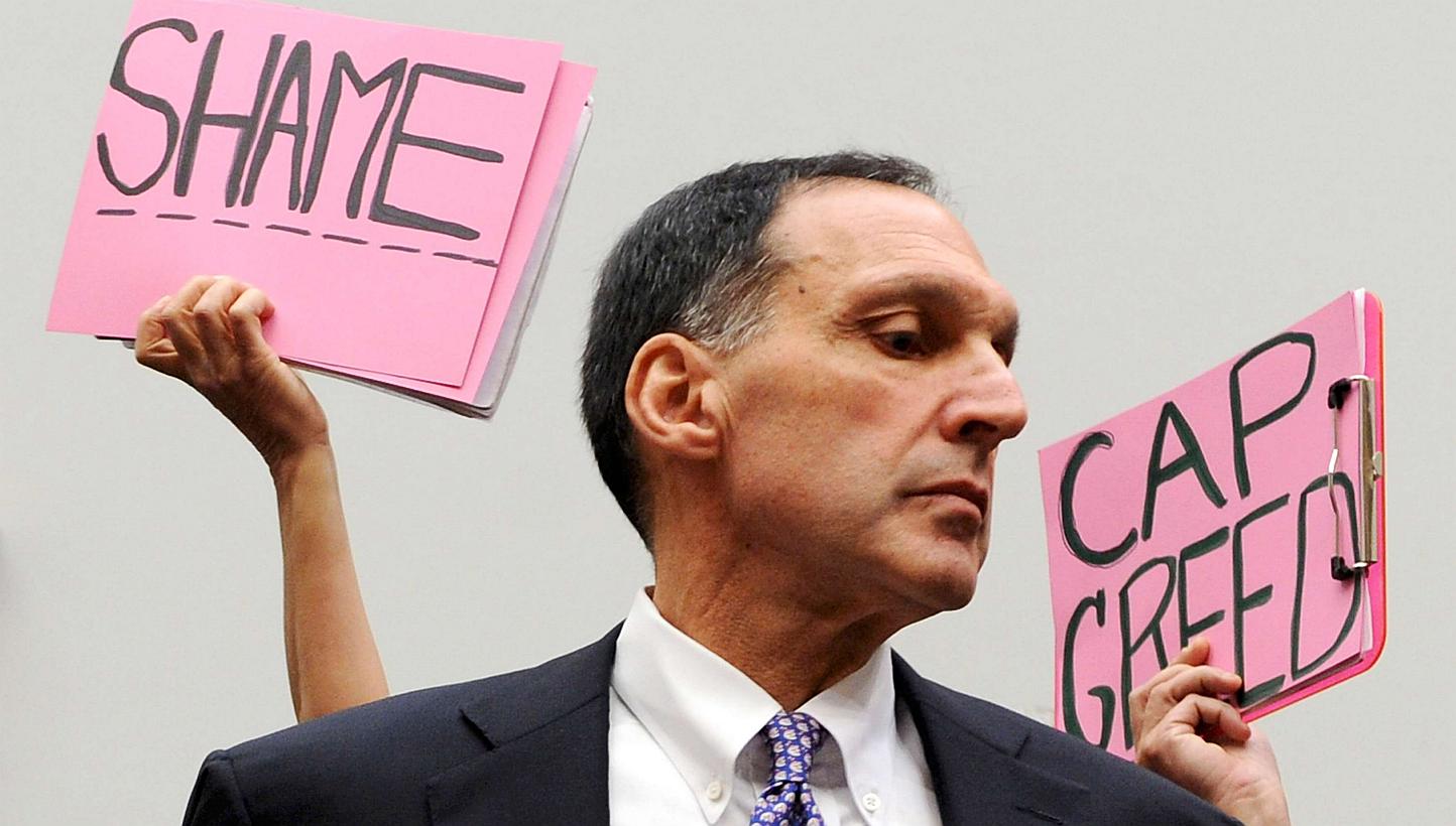 Protestors holding signs behind Richard Fuld as he takes his seat to testify at a House Oversight and Government Reform Committee hearing on the causes and effects of the Lehman Brothers bankruptcy, on Capitol Hill in Washington in this Oct 6, 2008 f