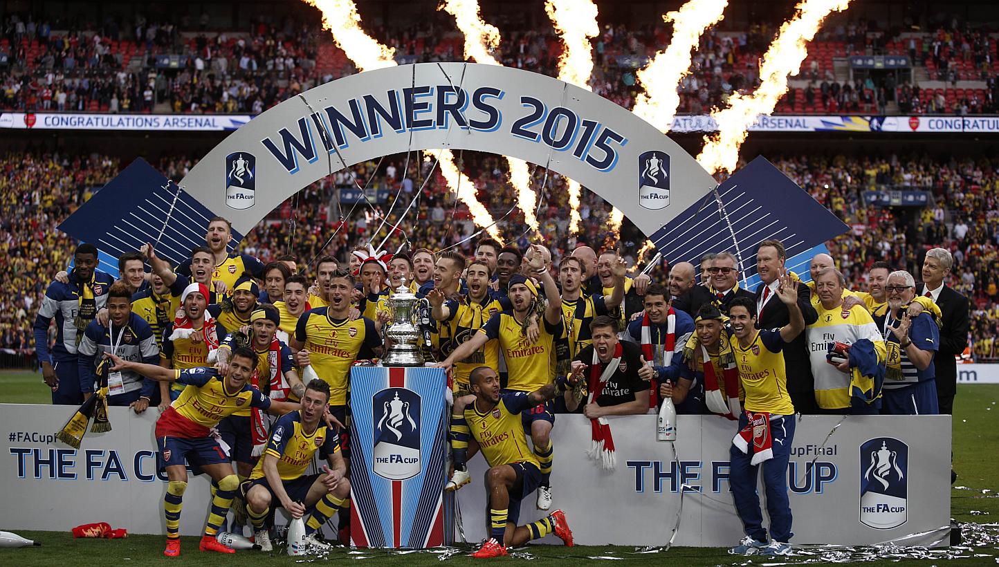 Arsenal manager Arsene Wenger (right) watches as his team celebrate with the trophy after winning the FA Cup final football match between Aston Villa and Arsenal at Wembley stadium in London on May 30, 2015. -- PHOTO: AFP