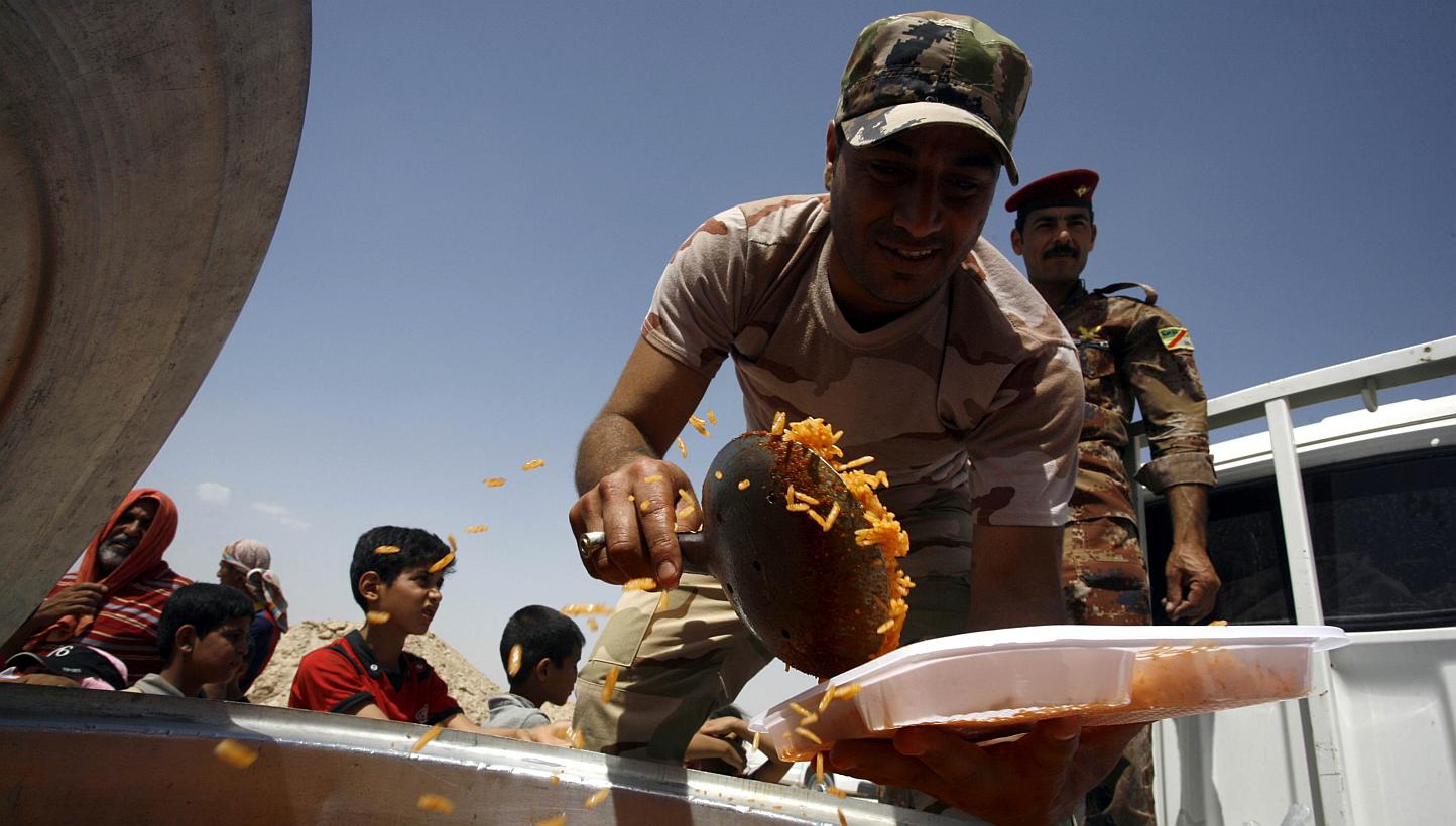 A member of the Iraqi government forces distributes food to displaced Iraqis who fled Anbar province due to the ongoing conflict between pro-government forces and Islamic State (IS) group jihadists, at a makeshift camp for internally displaced person