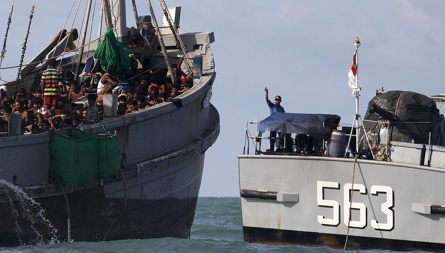 A Myanmar military officer (right) gestures from a navy ship towards a boat packed with migrants, off Leik Island in the Andaman Sea on&nbsp;May 31, 2015. Myanmar's navy is escorting a boat crammed with 727 abandoned migrants to the waters of neighbo