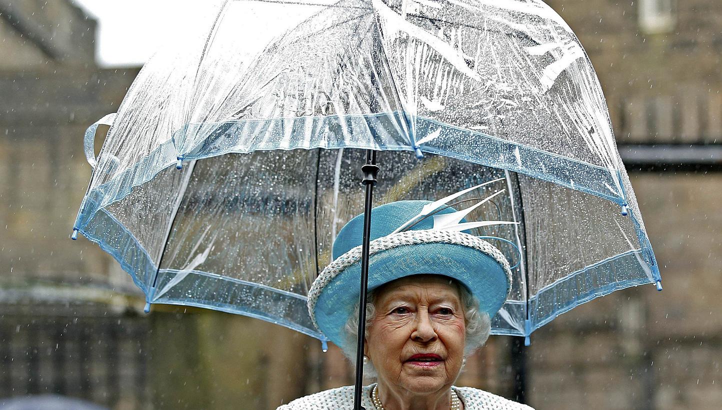 Britain's Queen Elizabeth II shelters from the rain beneath an umbrella as she arrives at Lancaster Castle in Lancaster, northern England on May 29, 2015. -- PHOTO: AFP&nbsp;