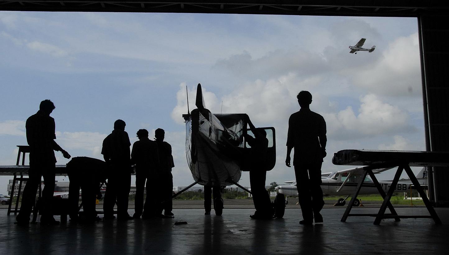 A Cessna aircraft taking off in the background as engineers work on assembling a training plane at an academy at Shirpur airport in rural Maharastra, India, in 2006. Dozens of pilots in India have certificates showing inflated flying hours and ground