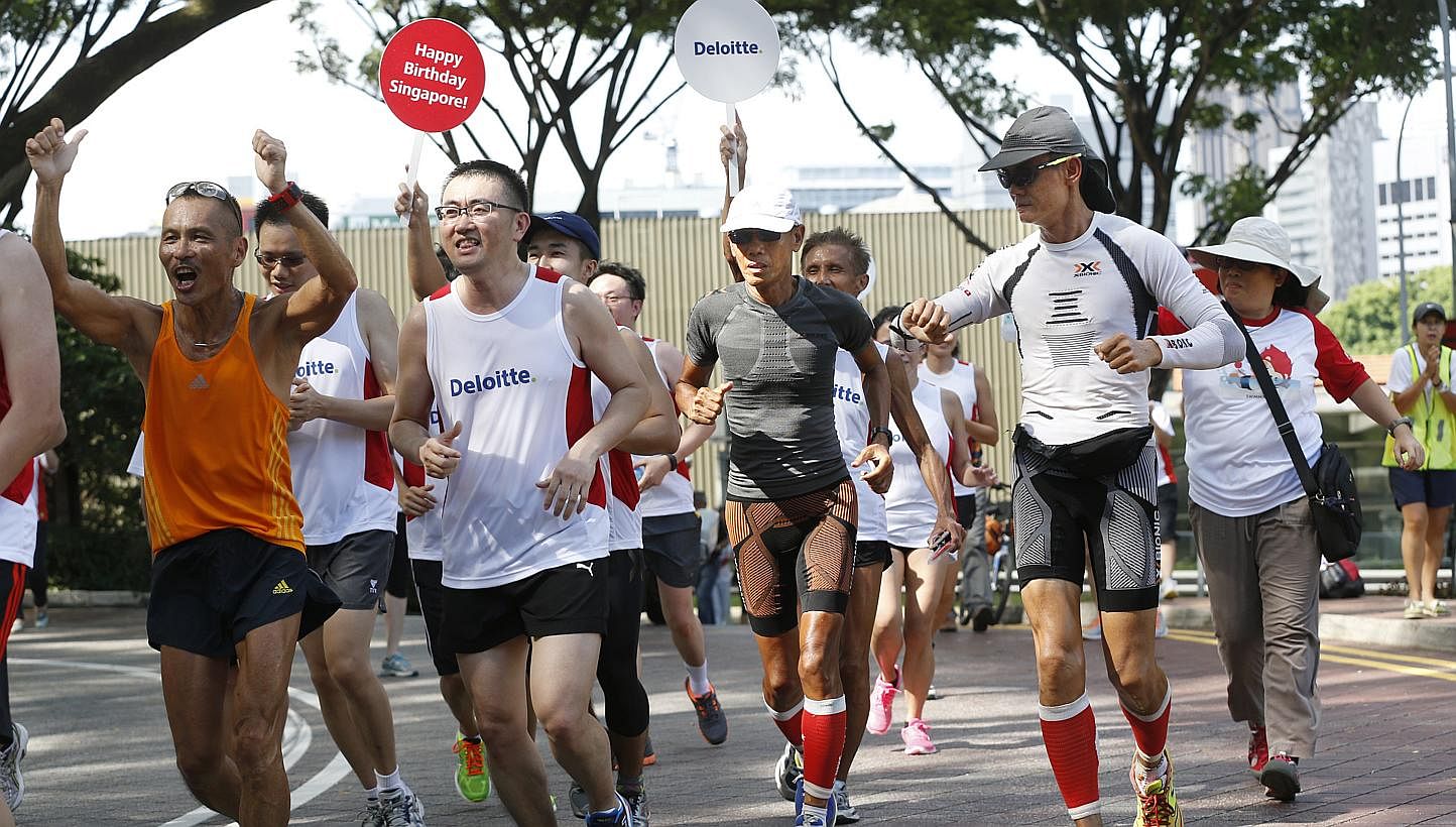Ultramarathoners Lim Nghee Huat (in grey) and Yong Yuen Cheng (in white long-sleeved shirt), with representatives from Deloitte, finishing their 49th leg at Fort Canning Park yesterday. The pair's support crew follow behind them, stopping every kilom