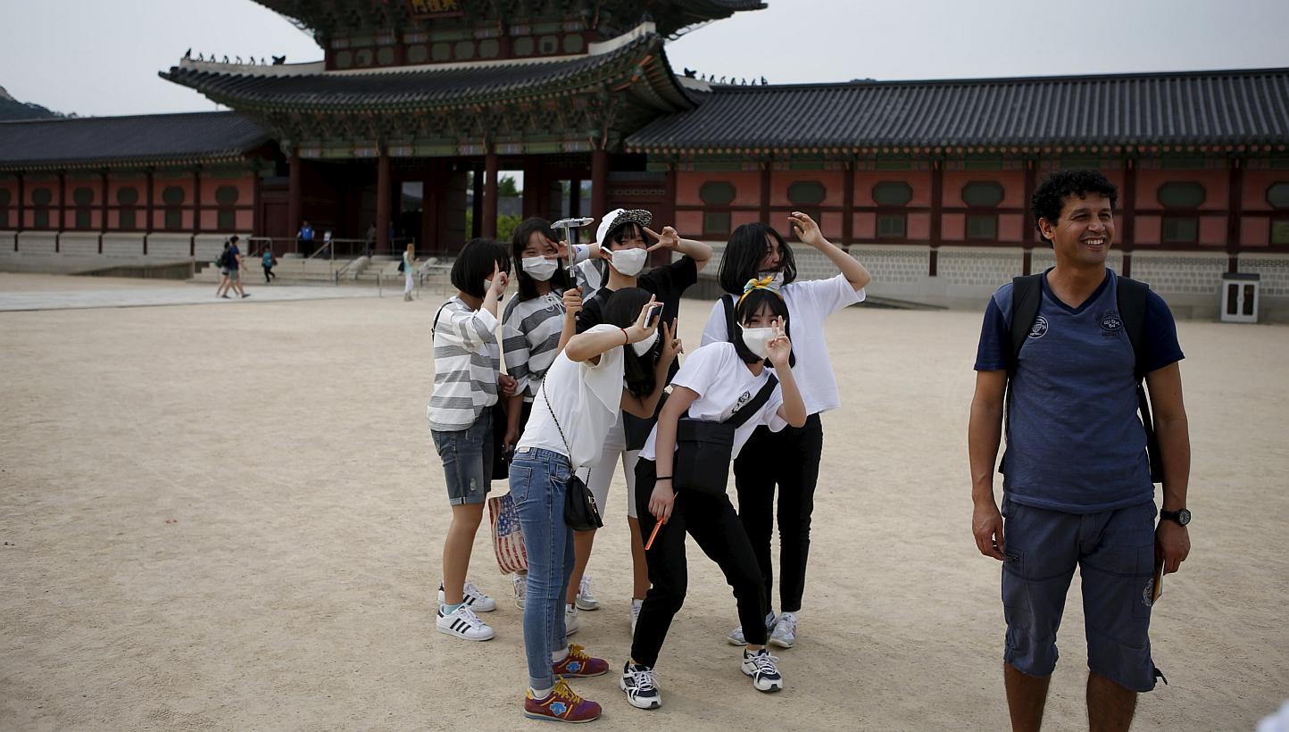 South Korean students wearing masks to protect against the Middle East Respiratory Syndrome (Mers) standing behind a tourist as he poses for photographs at the Gyeongbok Palace in central Seoul on June 4, 2015. -- PHOTO: REUTERS&nbsp;