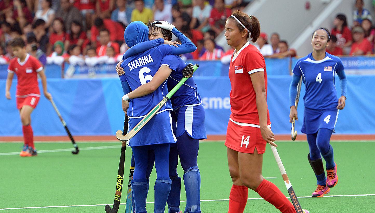 Singapore's Toh Limin walking past her jubilant Malaysian opponents after the women's hockey team was hammered 7-0 in their SEA Games opener at Sengkang hockey stadium on June 6, 2015. -- ST PHOTO: DESMOND WEE