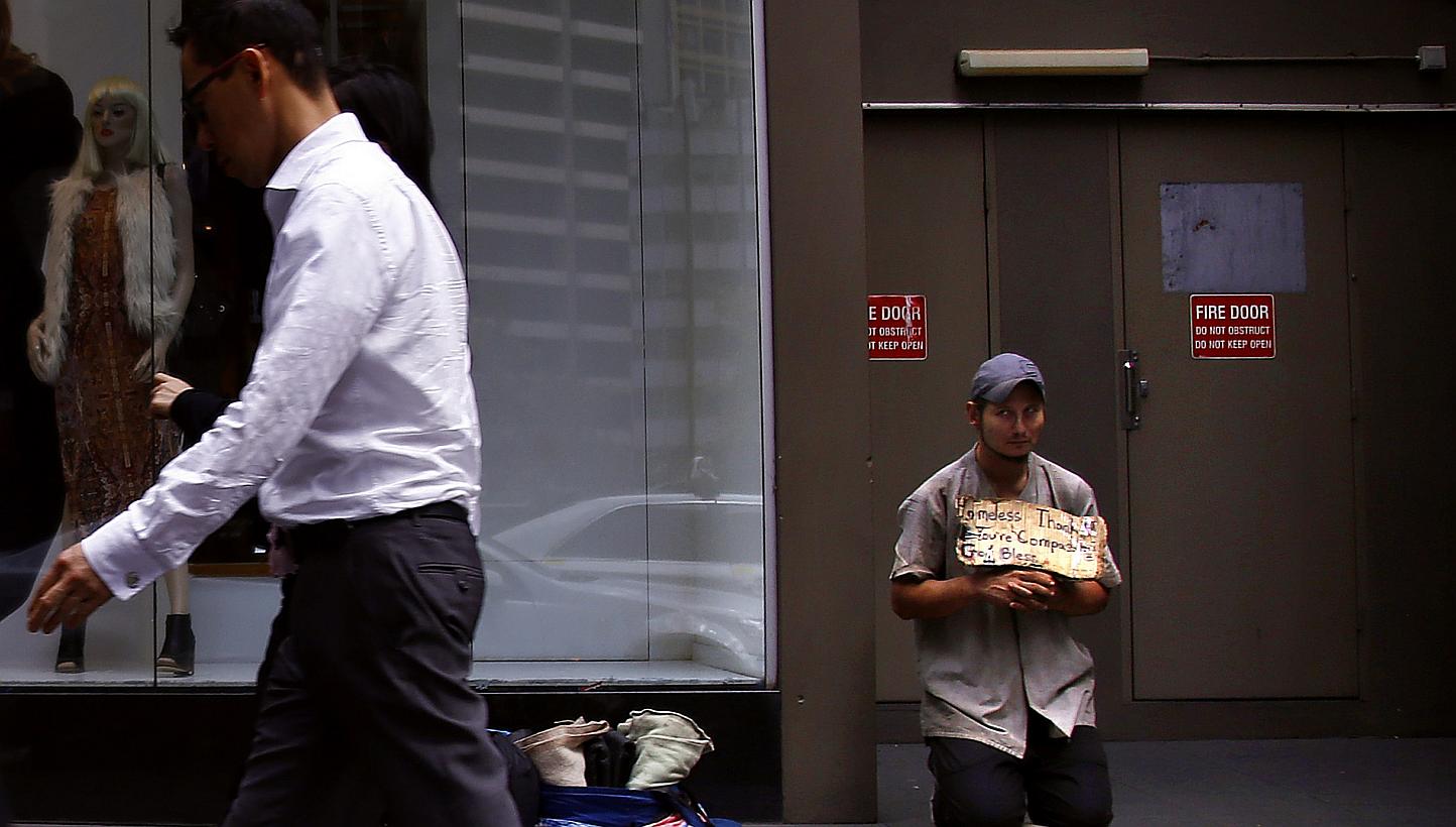 A pedestrian walks past a man holding a sign as he begs for money on a main street in central Sydney on March 18, 2015. Australian unemployment unexpectedly fell in May to the lowest in a year, indicating that improved business confidence is translat