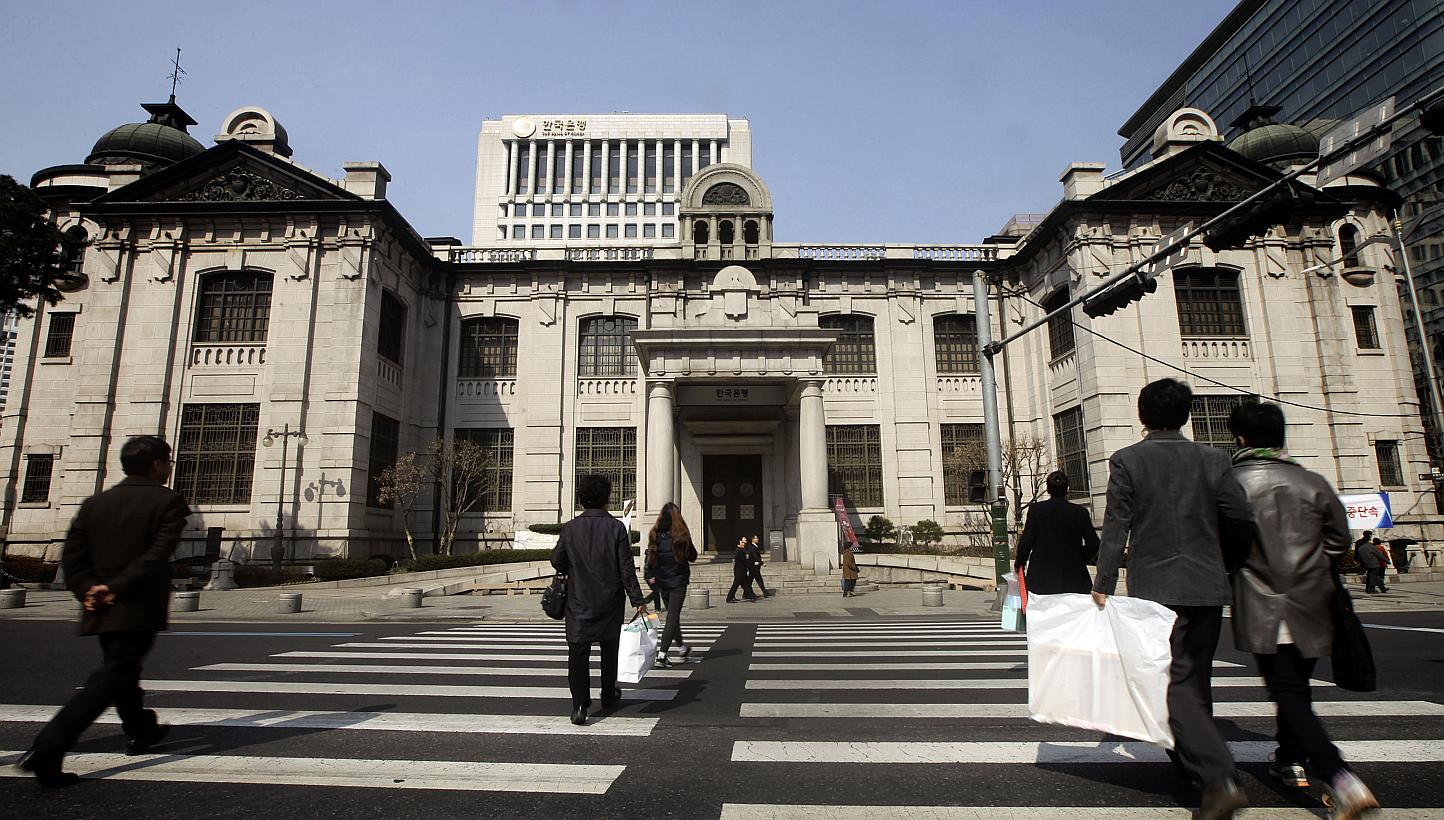 Pedestrians cross a road in front of the Bank of Korea headquarters in Seoul, South Korea, on Monday, March 3, 2014. South Korea's central bank cut its policy rate by 25 basis points to a record-low 1.50 per cent on Thursday to offset any potentially