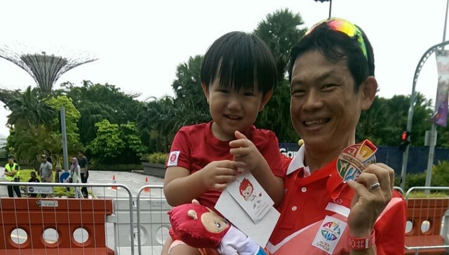 Singapore cyclist Vincent Ang, carrying his son Joshua, with his SEA Games bronze medal in the men's criterium on June 12, 2015. -- ST PHOTO: HO SI RUI&nbsp;