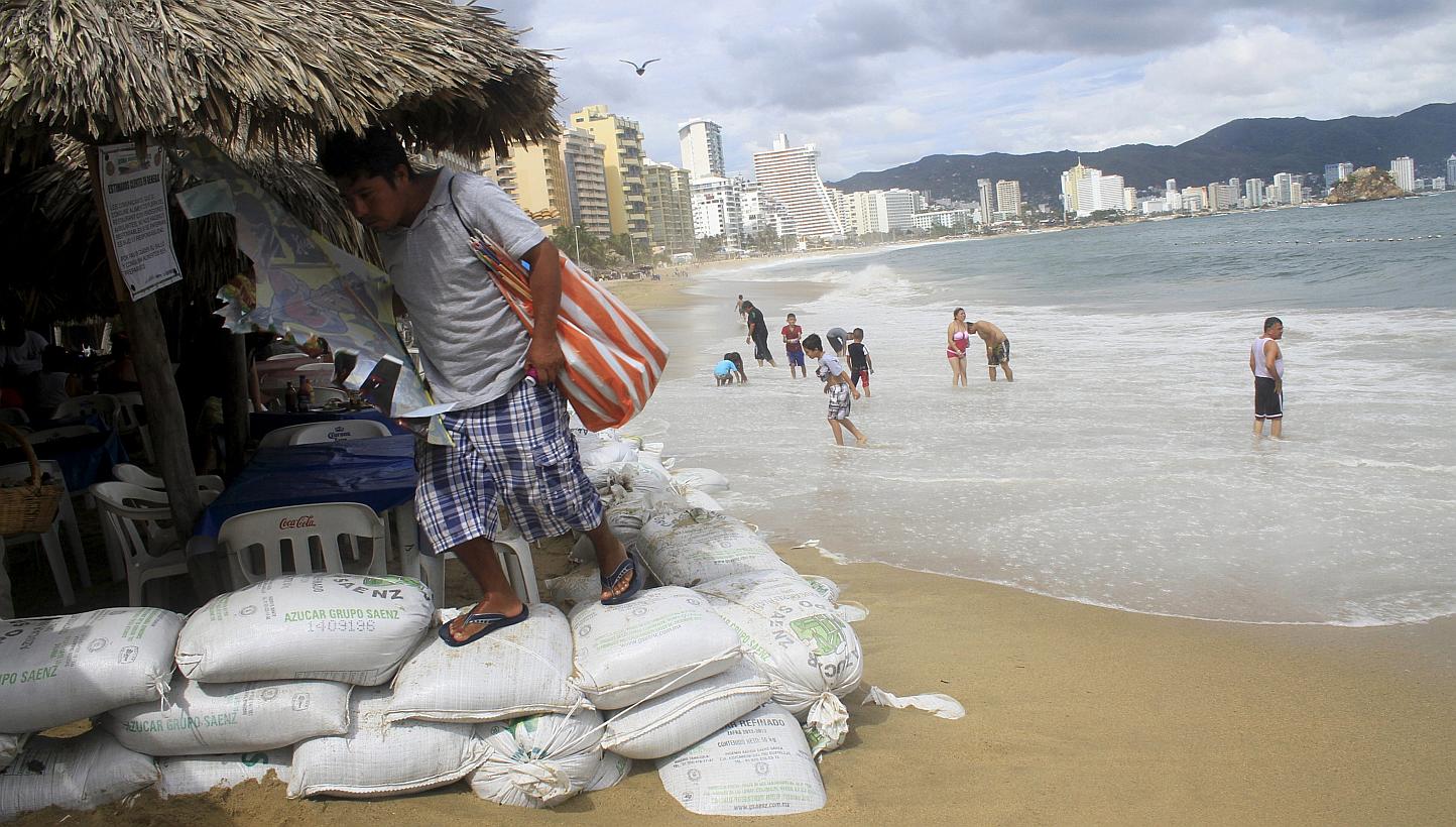A vendor walks over sand bags placed by the personnel of a restaurant at a beach as dark clouds brought by the proximity of tropical storm Carlos are seen in Acapulco, June 12, 2015. -- PHOTO: REUTERS