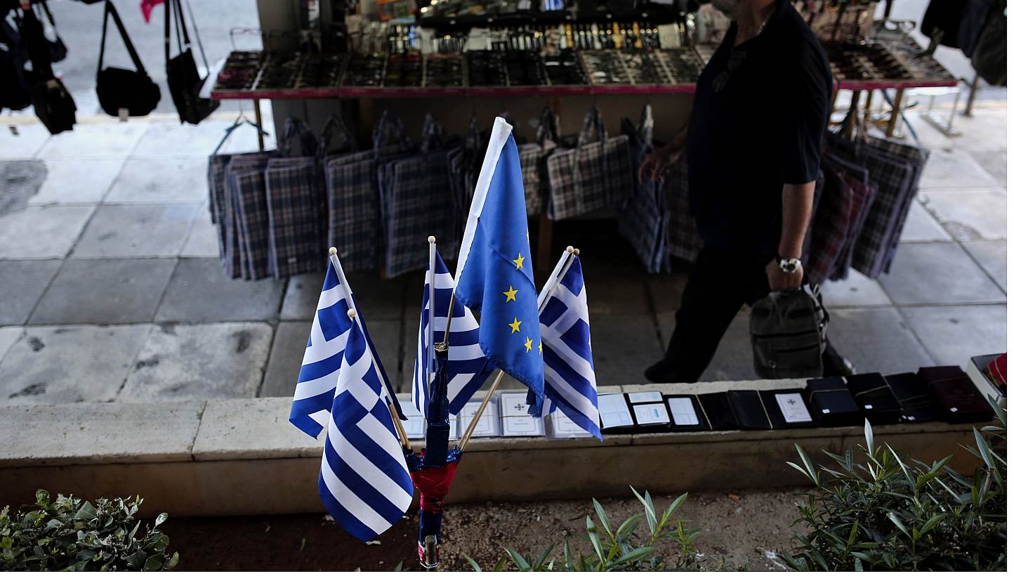 A man walks next to Greek national and European Union flags near the port of Piraeus on June 14, 2015. Greek and EU-IMF negotiators were locked in last-chance talks on Sunday to avert a default by Athens that could pave the way for a catastrophi