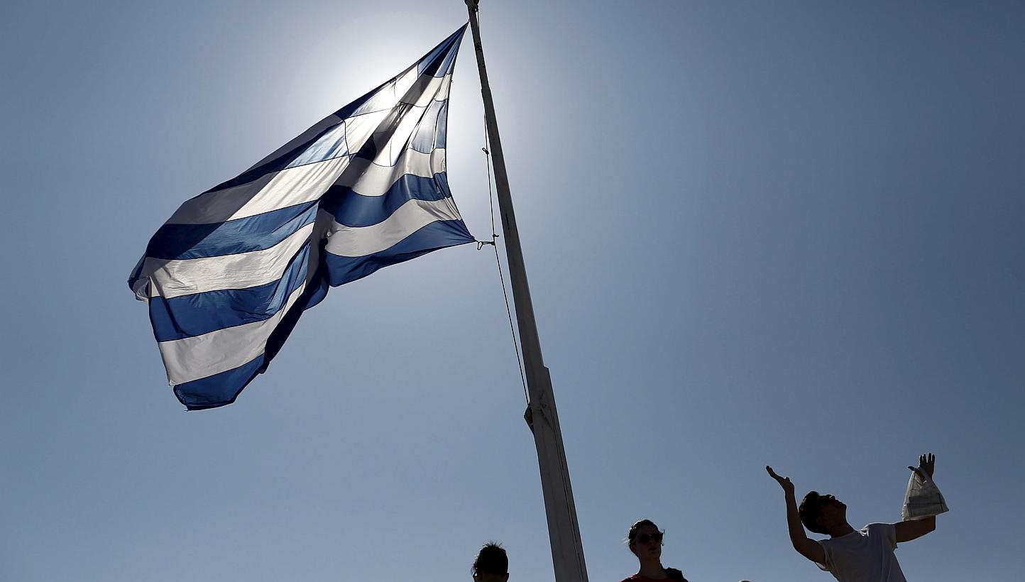 Tourists stand under a Greek national flag atop the Acropolis hill in Athens, on June 14, 2015. Talks on ending a deadlock between Greece and its international creditors broke up in failure on Sunday, with European leaders venting their frustration a