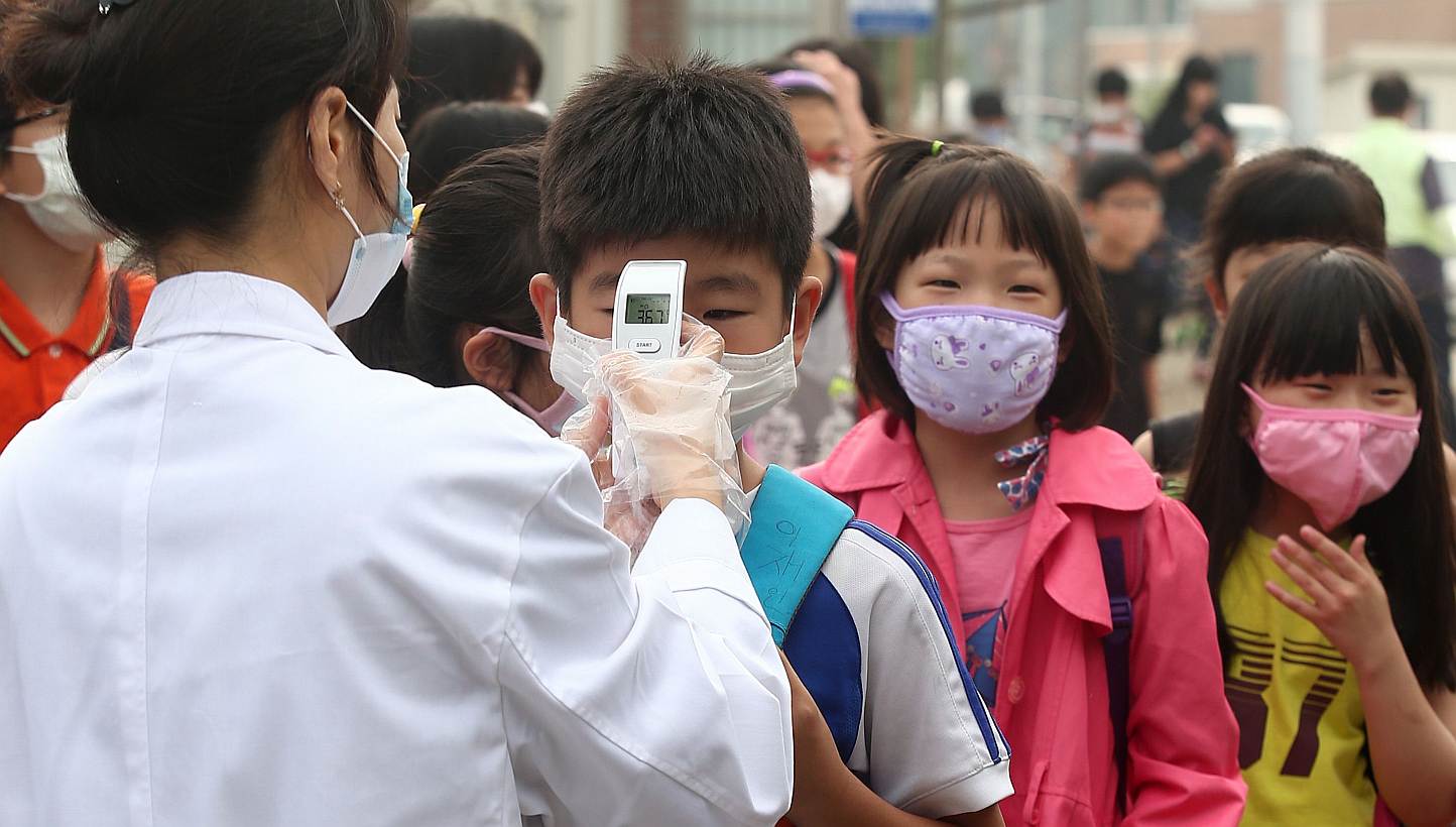 A health worker checks the body heat of children wearing face masks at an elementary school in Pyeongtaek, 65km south of Seoul, on June 15, 2015 as the school is reopened after a temporary closure in response to public fears over Middle East Respirat