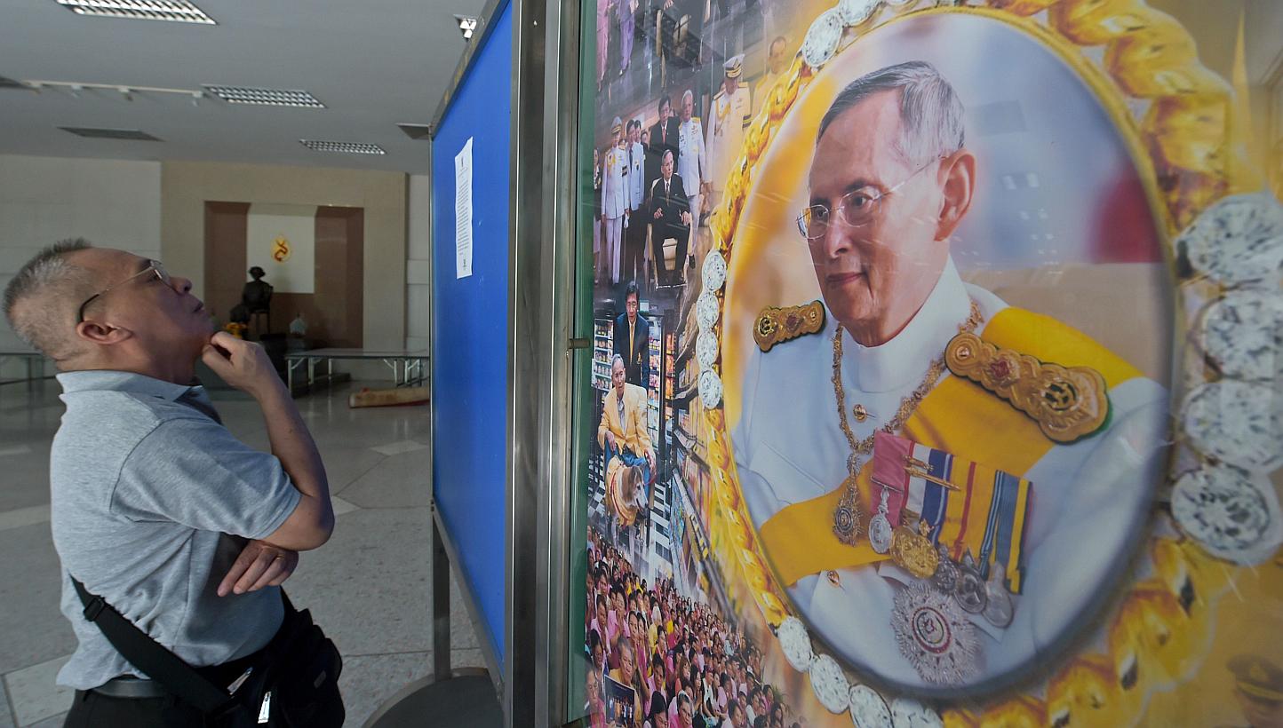 A Thai well-wisher reads a statment from the royal bureau next to a portrait of Thai King Bhumibol at Siriraj hospital in Bangkok on June 1, 2015. Thailand's junta has banned a journalists' association from holding a debate on controversial lese maje