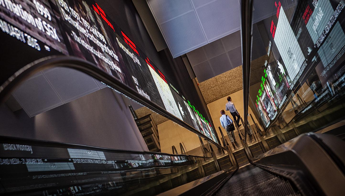Pedestrians exit an escalator that runs past an electronic screen and ticker board that indicates stock figures at the Singapore Exchange (SGX) headquarters in Singapore, on Jan 21, 2015. -- PHOTO: BLOOMBERG&nbsp;