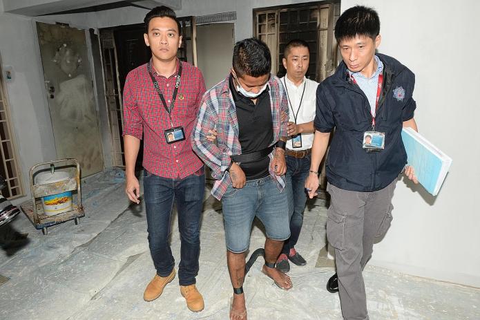 Police and the suspected arsonist at the scene of his alleged crime in Toh Guan Road yesterday. The man is said to have been involved in setting fire to two flats located above a client of a loanshark.