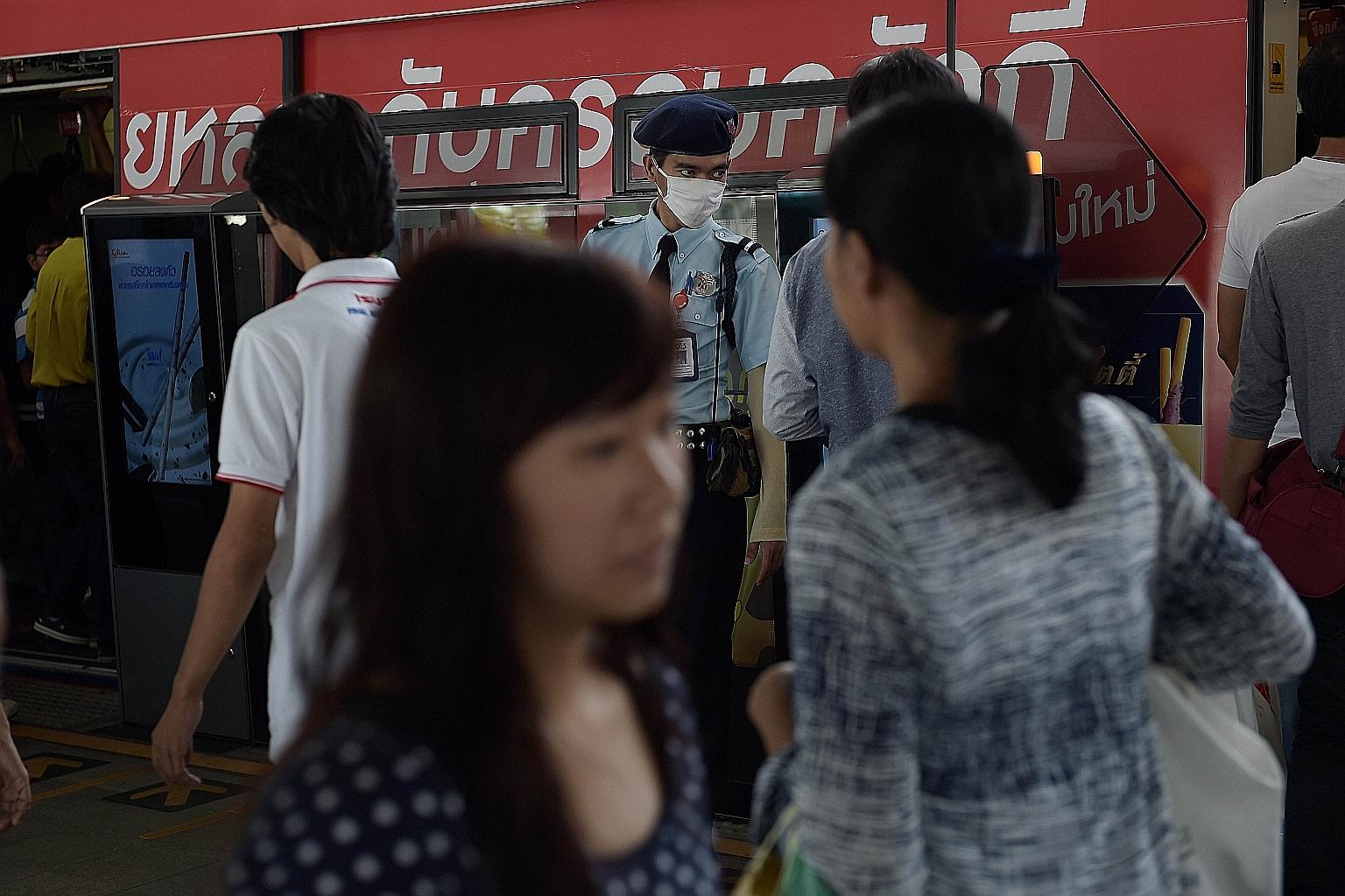 Commuters under the watchful eye of a security guard in a face mask at a Bangkok train station yesterday. Currently, 59 people are being monitored by the authorities for suspected Mers infection.